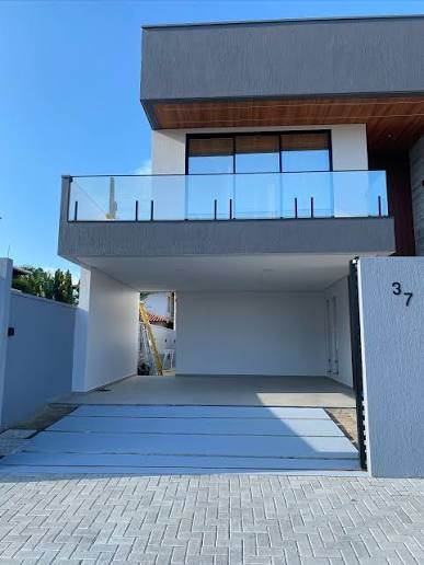 Nowoczesny dom z balkonem i garażem, wykończony w szarościach. Widoczny fragment elewacji z numerem 37 i brama wjazdowa z kostki brukowej.