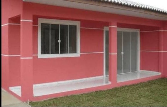 Różowa elewacja domu z białymi akcentami: okno z kratami i przeszklone drzwi balkonowe. Świeżo pomalowana ściana i podłoga balkonu. Widok z zewnątrz na trawnik.