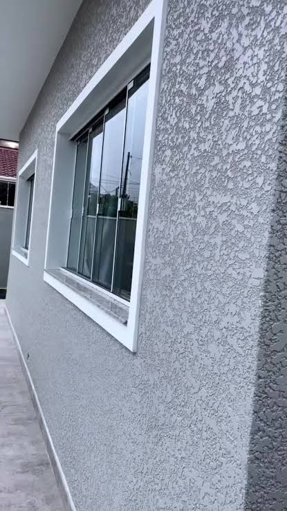 Szara elewacja budynku z oknami z białymi ramami. Widoczna faktura tynku baranka. Ujęcie z dołu, podkreślające strukturę ściany i detale wykończenia.