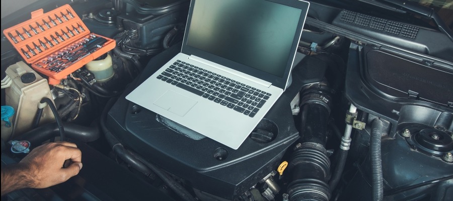 Diagnostyka samochodowa: Otwarta maska auta, laptop na silniku, zestaw narzędzi i dłoń mechanika. Widok z góry, ciemne oświetlenie warsztatowe.