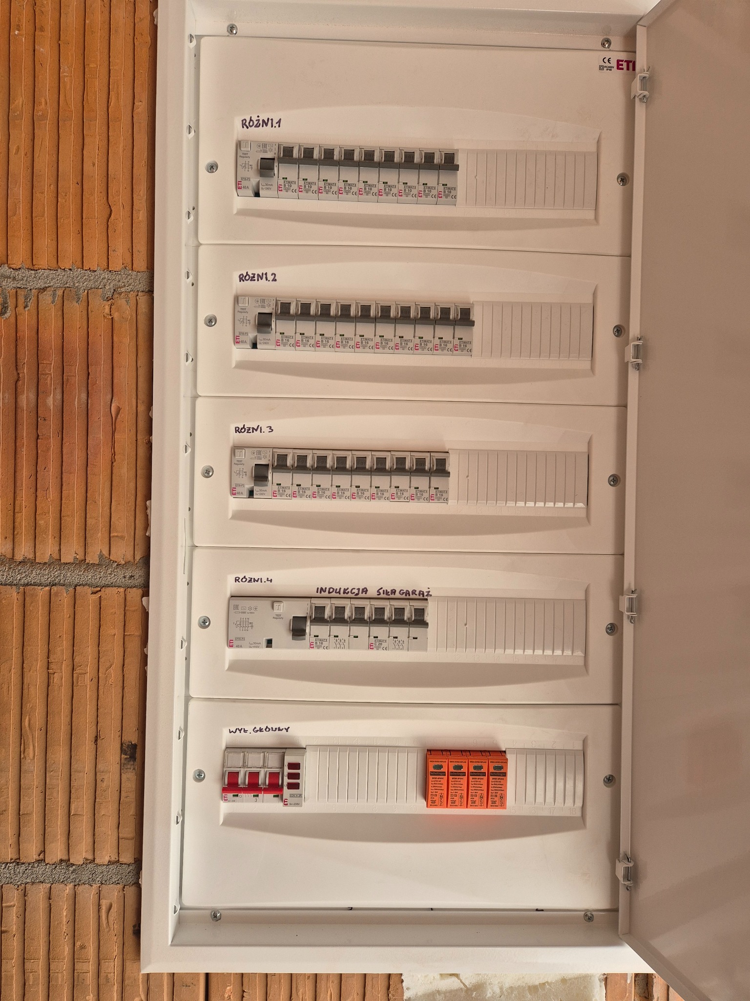 Rozdzielnica elektryczna z bezpiecznikami, zamontowana na ceglanej ścianie. Widoczne opisy obwodów: Różni.1, Różni.2, Różni.3, Indukcja Siła Garaż, Wył. Główny.