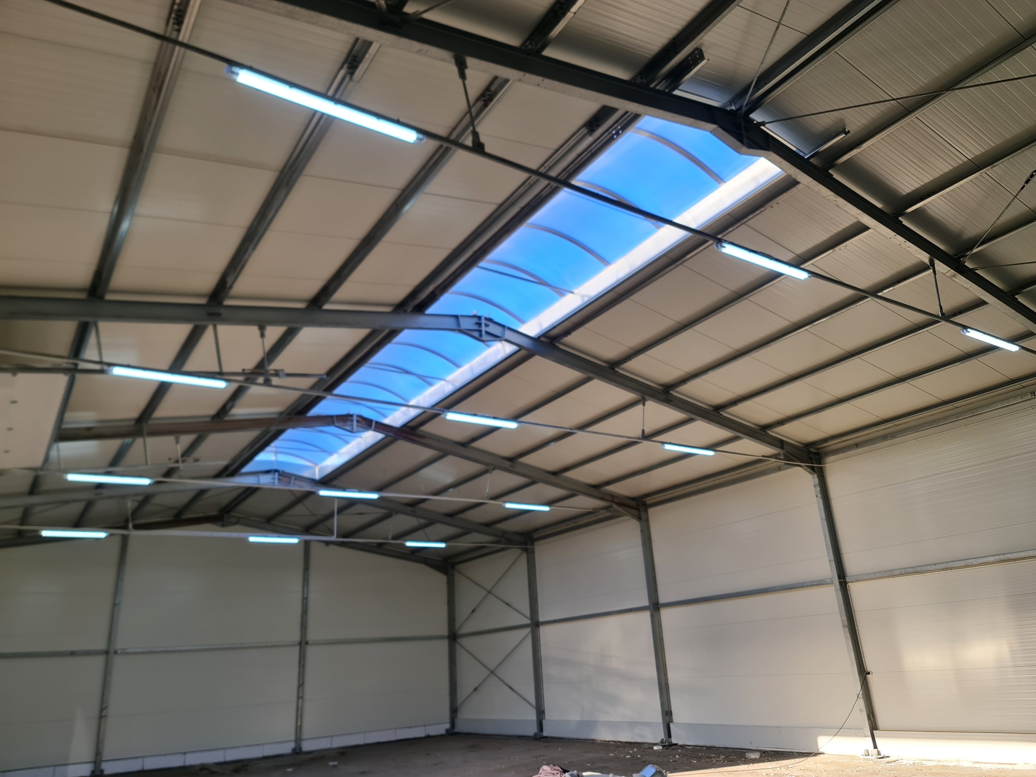 Wnętrze hali z zamontowanym oświetleniem LED i świetlikiem dachowym w Zduńskiej Woli. Widok na sufit z widoczną konstrukcją stalową i panelami ściennymi.