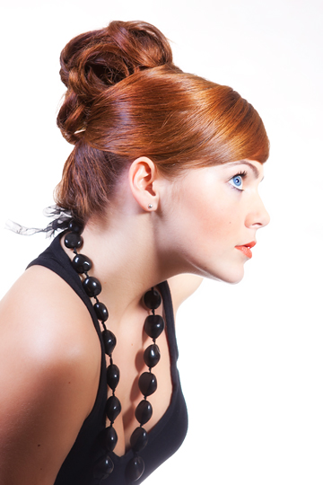 Portret kobiety z upiętymi rudymi włosami i makijażem, widok z profilu, czarne korale.