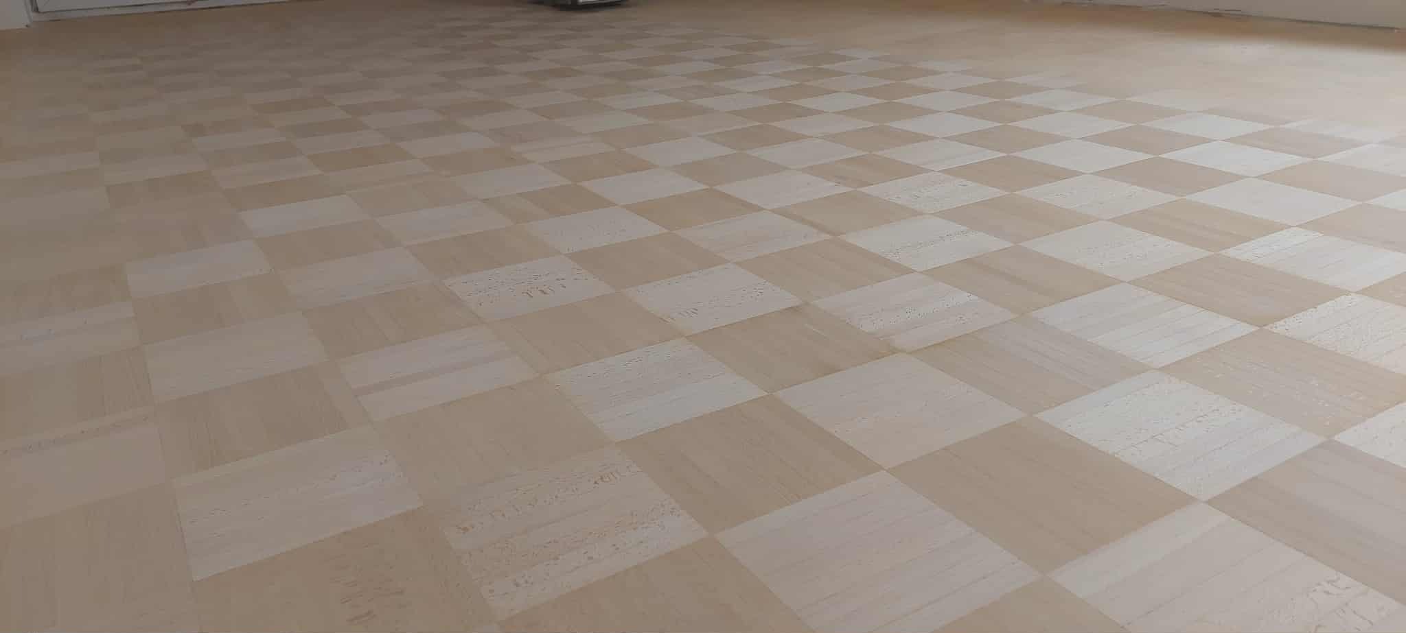 Parkiet ułożony w szachownicę z jasnego drewna, widok z perspektywy podłogi, delikatne oświetlenie podkreśla strukturę drewna.