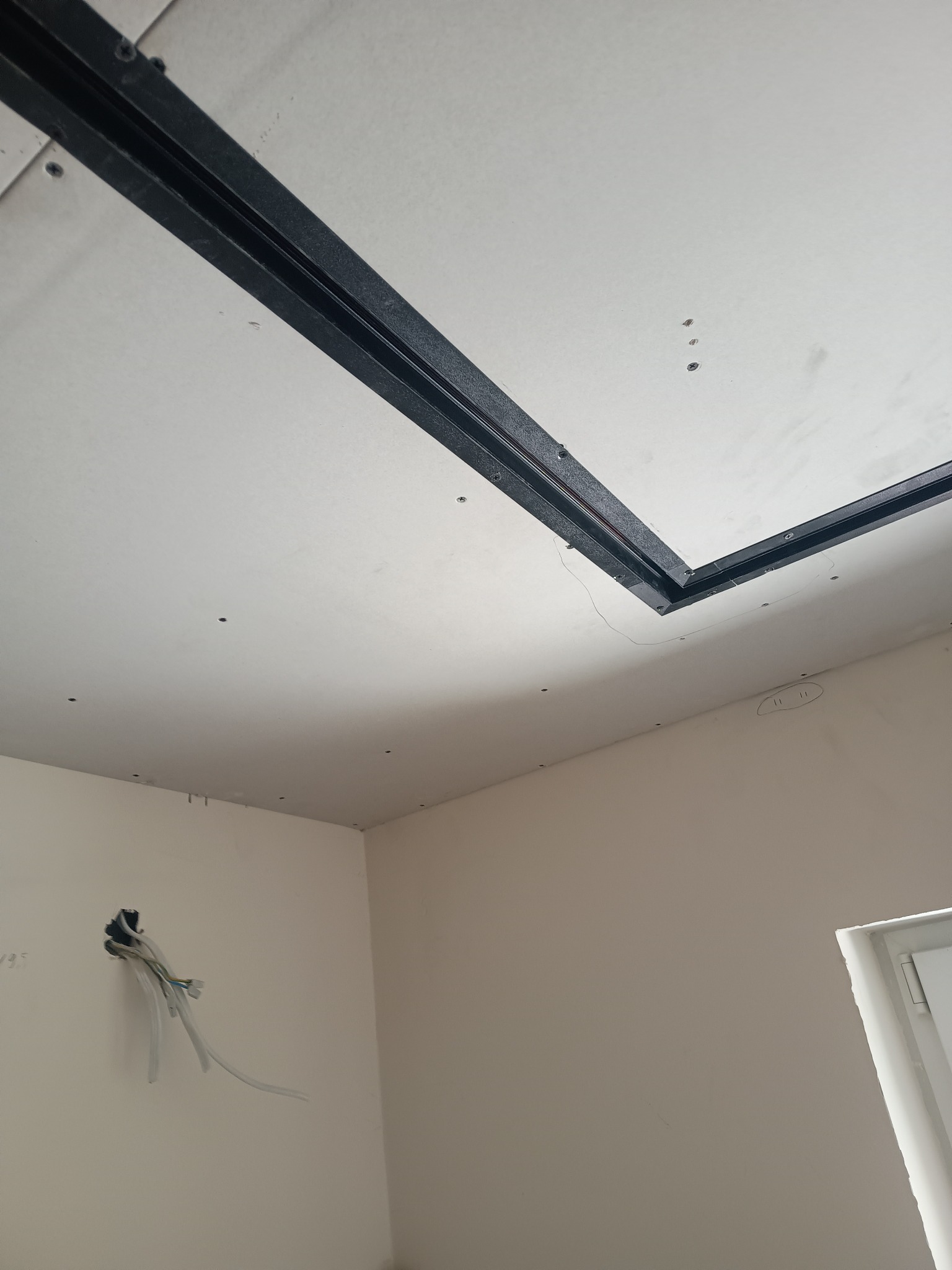 Sufit z płyt karton-gips z czarną ramą, widoczne kable w ścianie. Ujęcie z dołu, sufit w trakcie montażu, widoczne śruby mocujące.