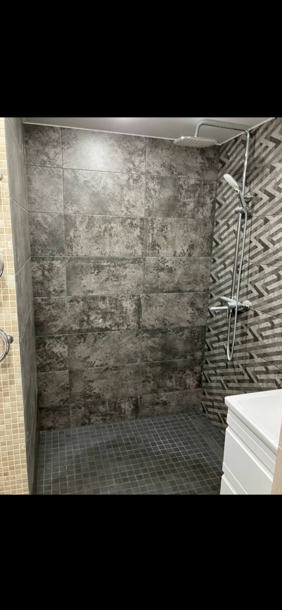 Wykończona kabina prysznicowa z szarymi płytkami imitującymi beton i geometrycznym wzorem. Widoczna bateria i odpływ liniowy. Nowoczesny design łazienki.