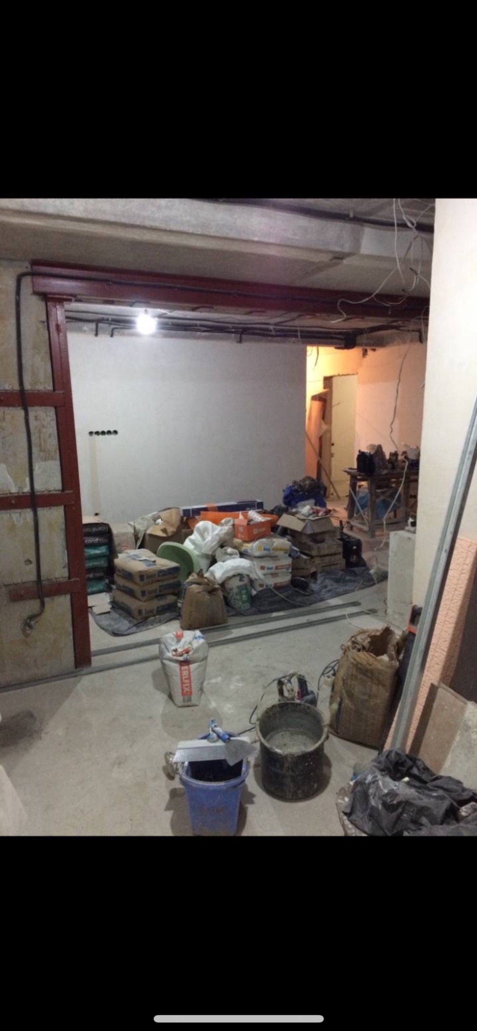 Wnętrze w trakcie remontu: worki z zaprawą, wiadra, narzędzia, widoczne instalacje elektryczne, surowy stan ścian i podłóg. Przygotowanie do prac wykończeniowych.