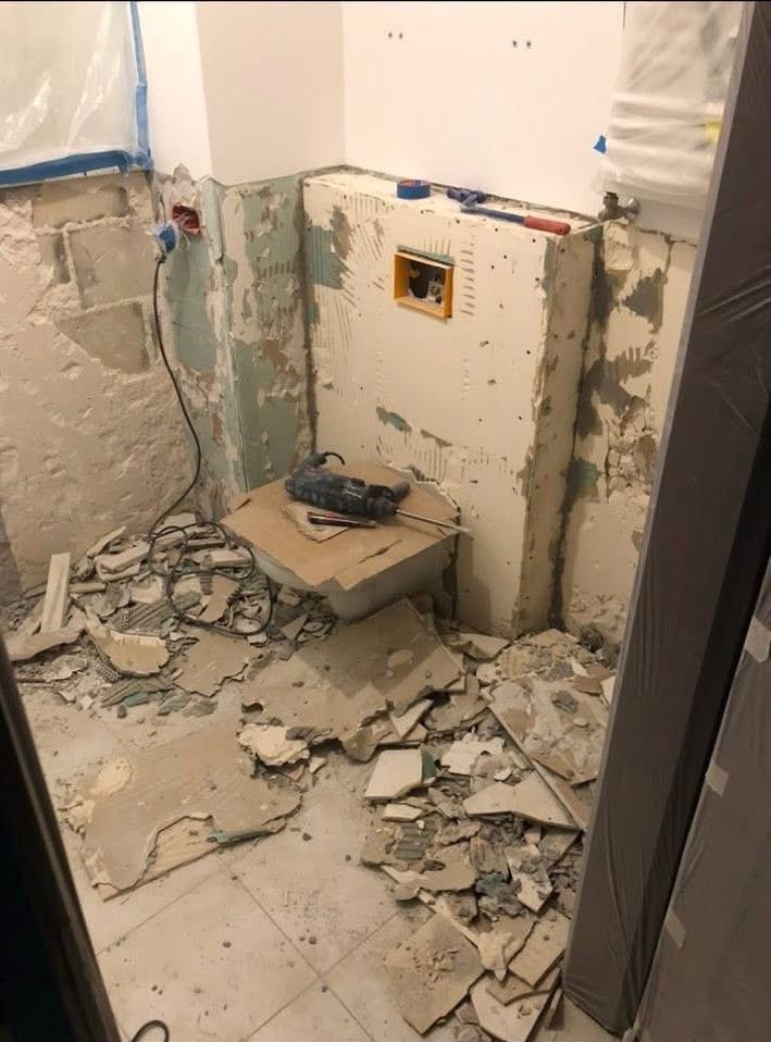 Demontaż płytek w łazience podczas remontu. Widoczne gruz, narzędzia i przygotowane ściany pod nowe wykończenie. Fragment instalacji w ścianie.