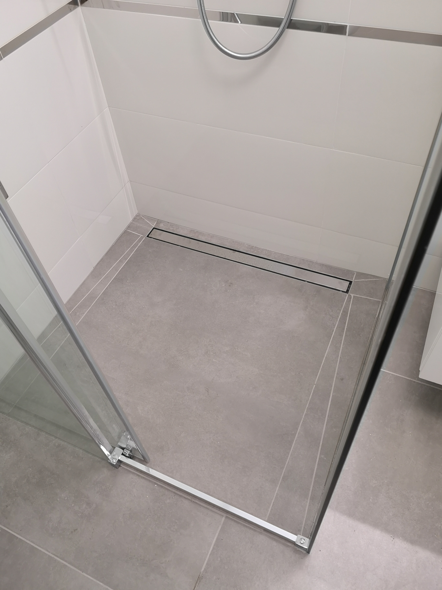 Nowoczesna kabina prysznicowa z odpływem liniowym i jasnymi płytkami. Minimalistyczny design, szklane drzwi i chromowane wykończenia. Widok z góry.