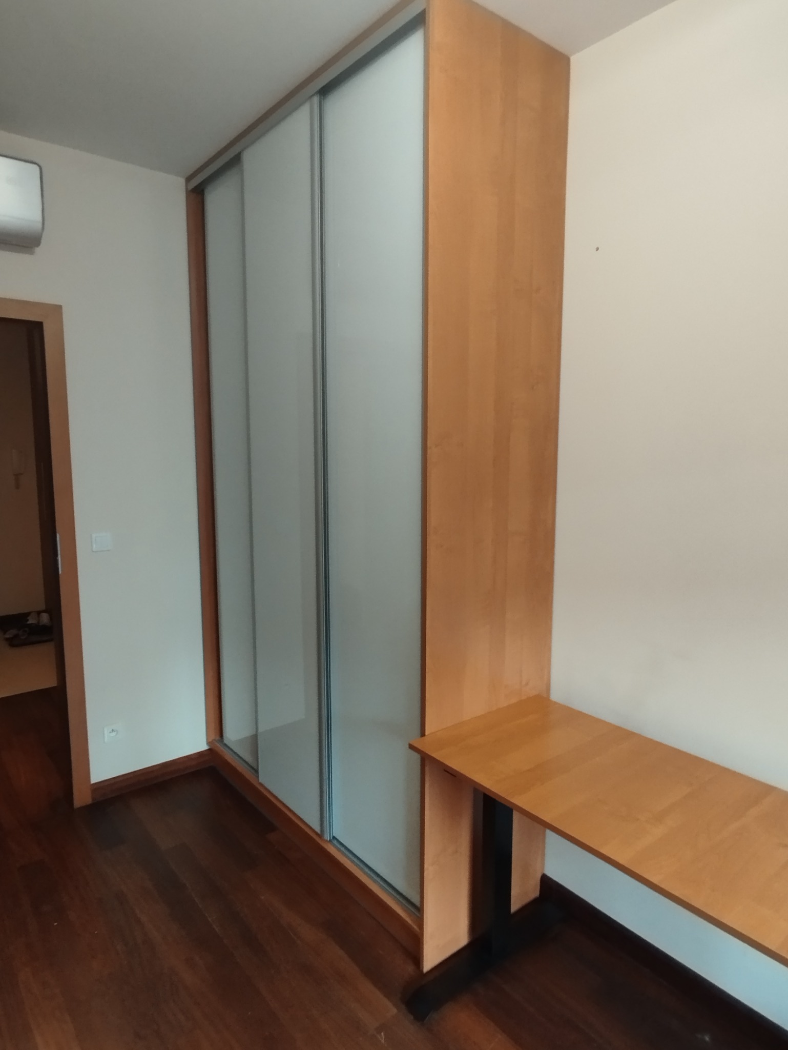 Jasna szafa przesuwna z biurkiem wbudowanym, drewniane wykończenie, minimalistyczny design, widok z boku, parkiet na podłodze, wnętrze pokoju.