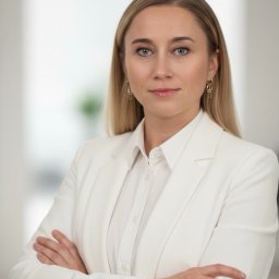 Kancelaria Adwokacka Adwokat Marta Bortel-Borowska - Portret kobiety w białym garniturze, z blond włosami i niebieskimi oczami, skrzyżowane ręce, delikatny uśmiech, jasne tło, profesjonalny wizerunek.