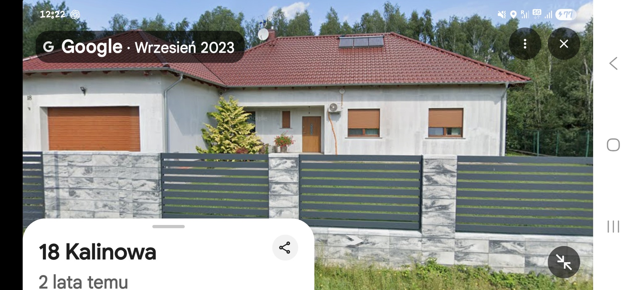 Dom jednorodzinny z czerwoną dachówką i szarym ogrodzeniem panelowym. Widoczne rolety zewnętrzne i klimatyzator. Zdjęcie z Google Street View.