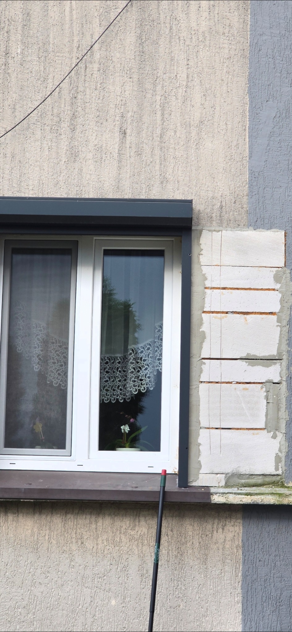 Okna z roletami zewnętrznymi w budynku z fragmentem ściany z bloczków, przygotowanej do prac wykończeniowych. Widoczne ślady po cięciu bloczków.