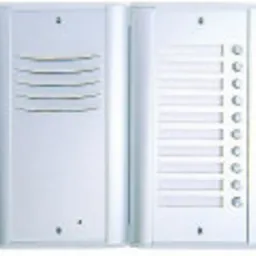 Panel domofonowy z przyciskami i głośnikiem, w obudowie z jasnego metalu, widoczne otwory na nazwiska lokatorów.