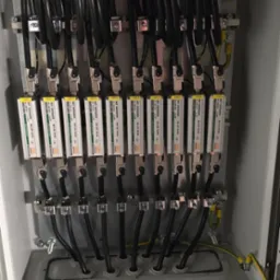 Rozdzielnica elektryczna z zainstalowanymi zabezpieczeniami przepięciowymi OBO Net Defender, widoczne przewody i listwy zaciskowe. Instalacja w szarej obudowie.