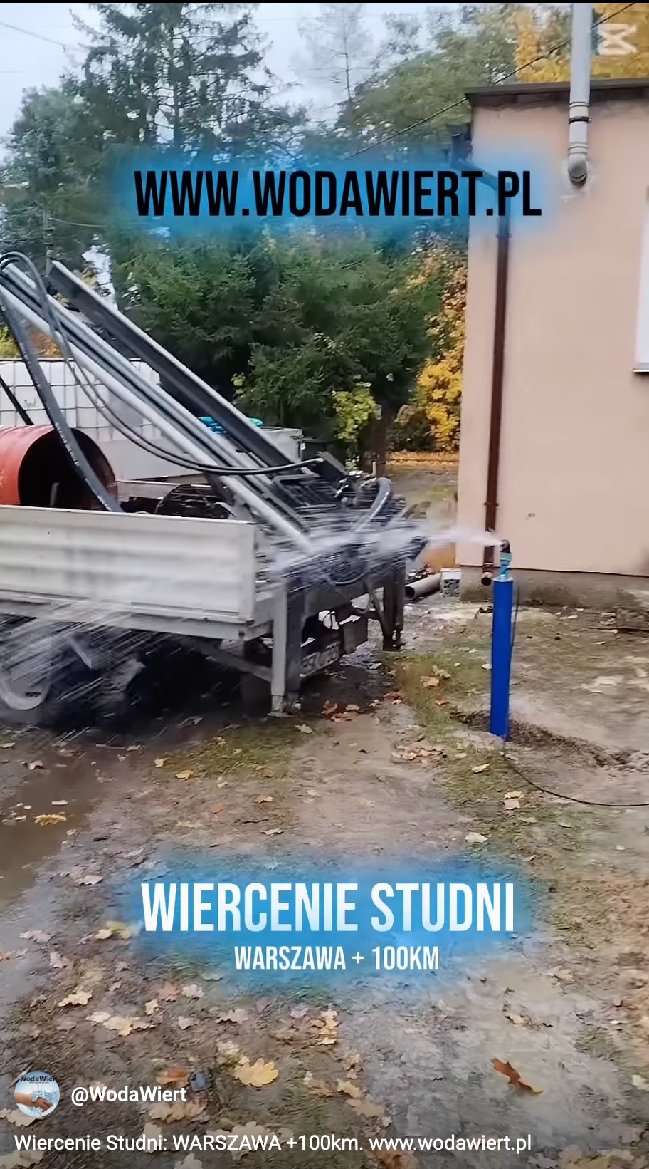 Wiercenie studni w toku: woda tryska spod wiertła zamontowanego na ciężarówce. W tle budynek i drzewa. Widoczne błoto i liście na ziemi.