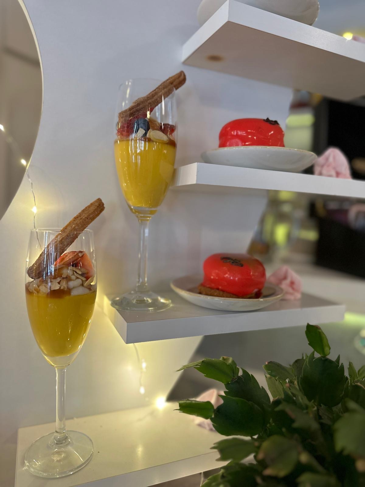 Eleganckie desery: mus w kieliszku z owocami i churro, czerwone ciastka na białych półkach, delikatne oświetlenie, nowoczesny minimalizm.