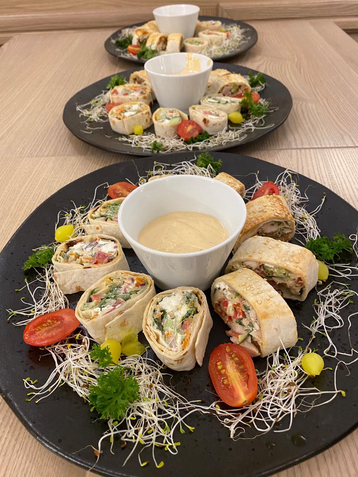 Dwa talerze z roladkami tortilli z różnymi nadzieniami, dipem, pomidorkami i kiełkami na drewnianym stole. Dekoracja potraw na przyjęcie.