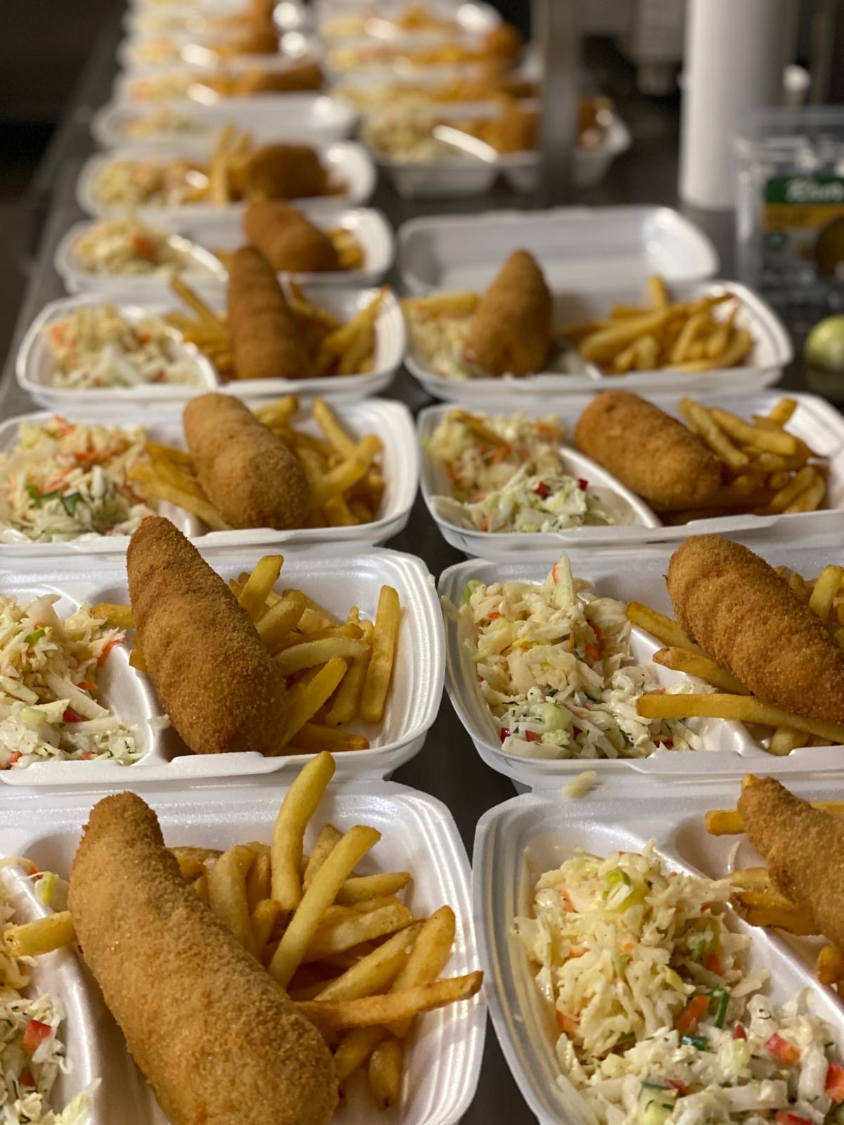 Porcje obiadowe w białych pojemnikach: krokiet, frytki i surówka. Gotowe zestawy cateringowe ułożone rzędami, widok z góry, oświetlenie naturalne.