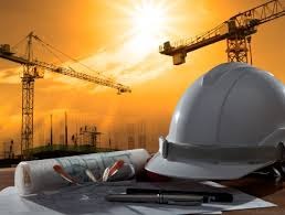 Plan budowy z kaskiem na pierwszym planie, w tle żurawie i zachodzące słońce w Lasocicach. Widok na projekt architektoniczny i narzędzia pracy.