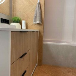 Mateusz Obarzanek Kompleksowe Wykończenia Wnętrz - Nowoczesna łazienka z drewnopodobnymi płytkami ułożonymi w jodełkę na ścianie i podłodze. Szafka pod umywalką z drewnianymi frontami i czarnymi uchwytami.