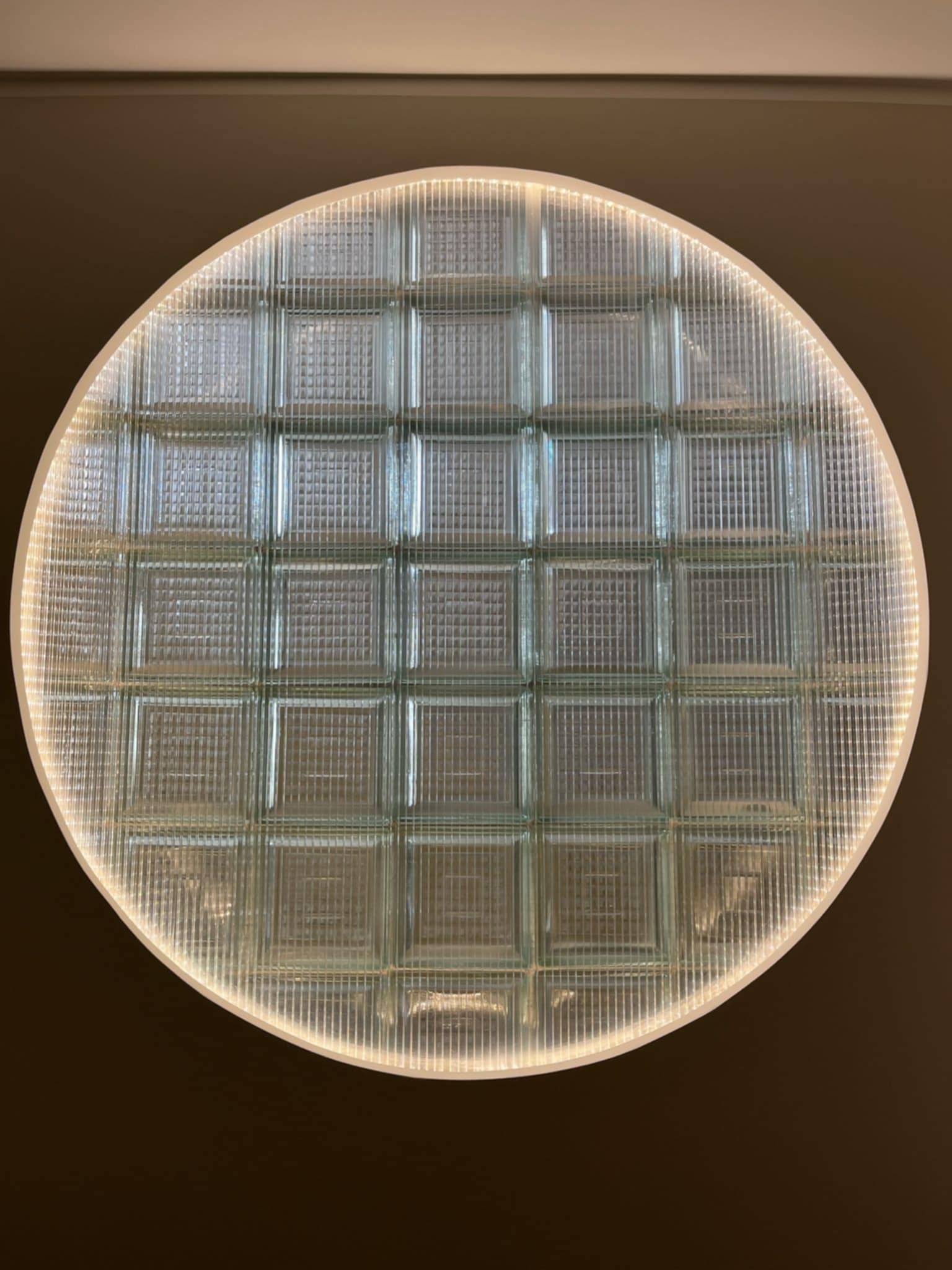 Okrągły świetlik z luksferów z podświetleniem LED na suficie. Widok z dołu, ukazujący strukturę szkła i równomierne oświetlenie.