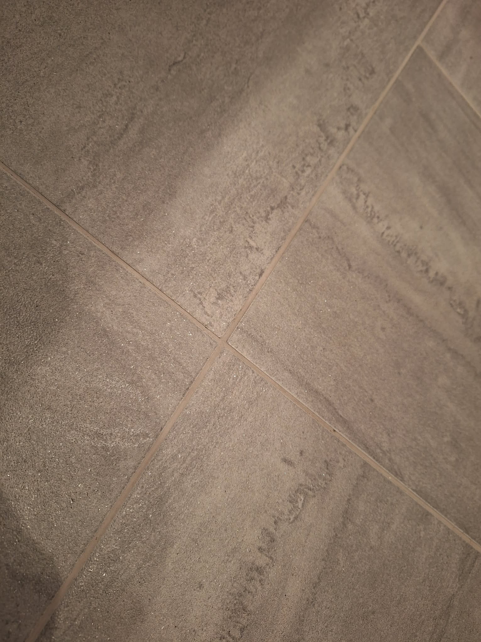 Szare, matowe płytki podłogowe ułożone w kwadraty, widoczne fugi. Delikatna struktura kamienia. Ujęcie pod kątem.