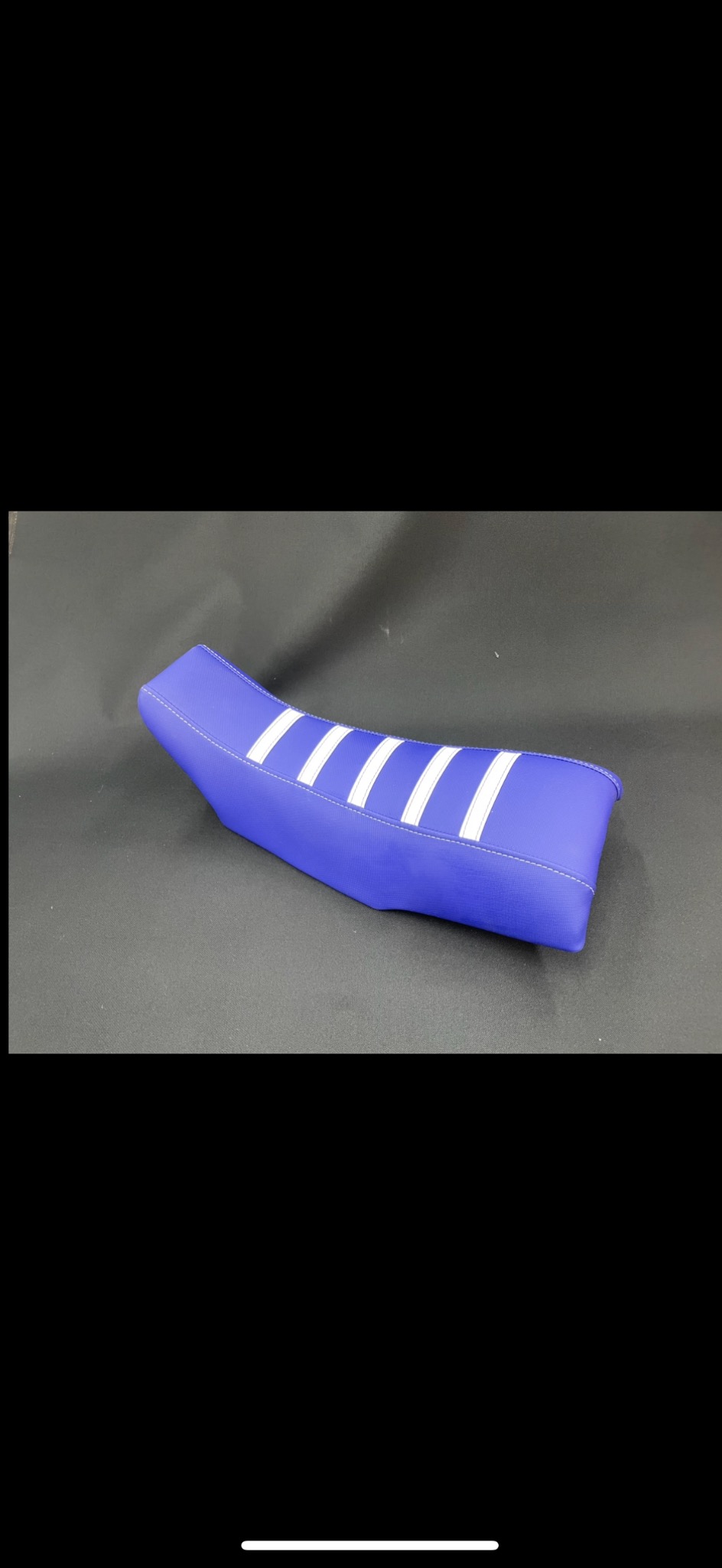 Niebieskie siedzenie motocyklowe z białymi pasami, świeżo po renowacji, leży na ciemnym tle. Widoczne precyzyjne szwy i dbałość o detale.