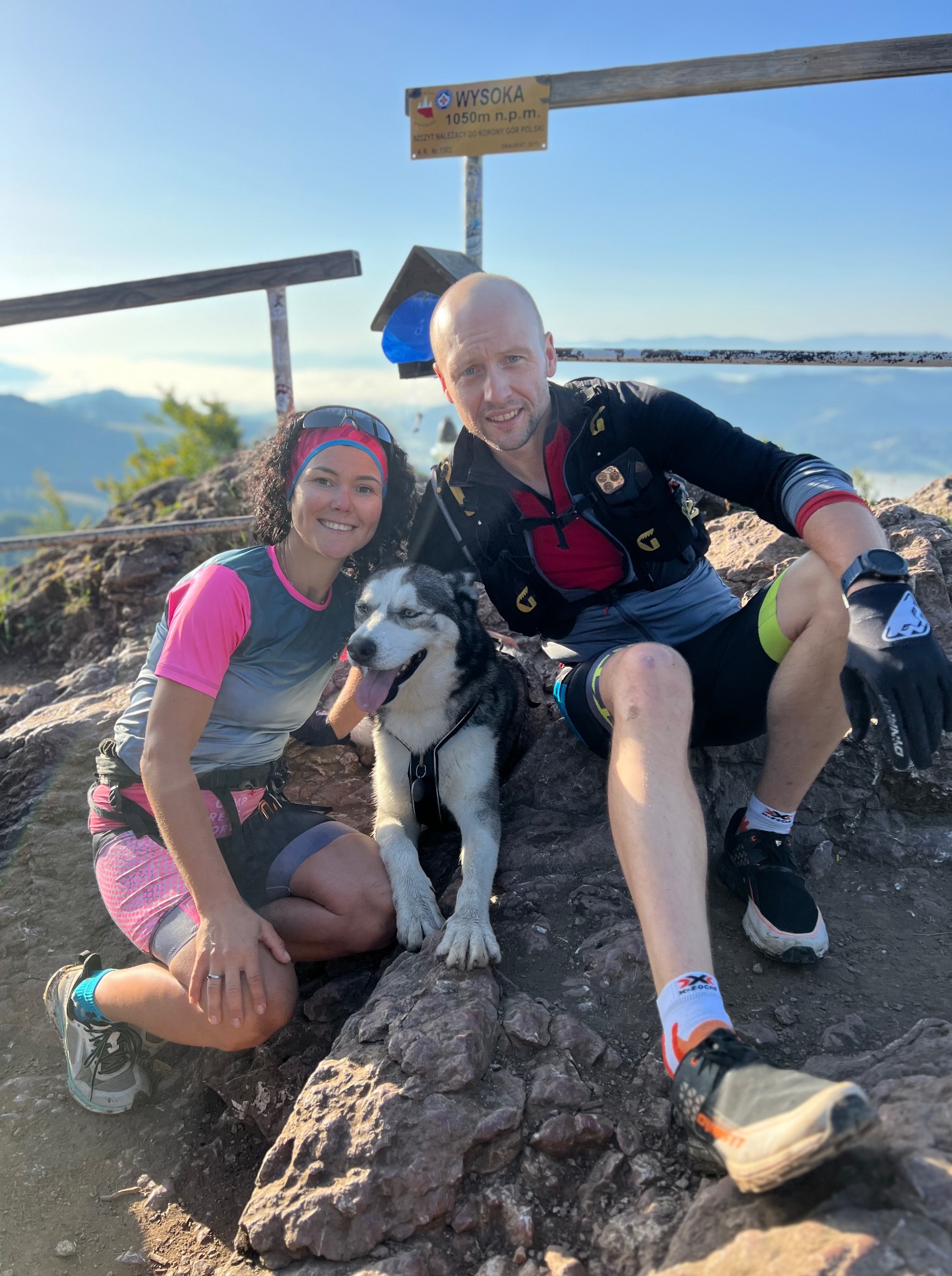 Para z psem husky na szczycie Wysoka w Pieninach, po treningu biegowym. Widok na góry, słoneczna pogoda. Trenerzy biegowi w strojach sportowych.