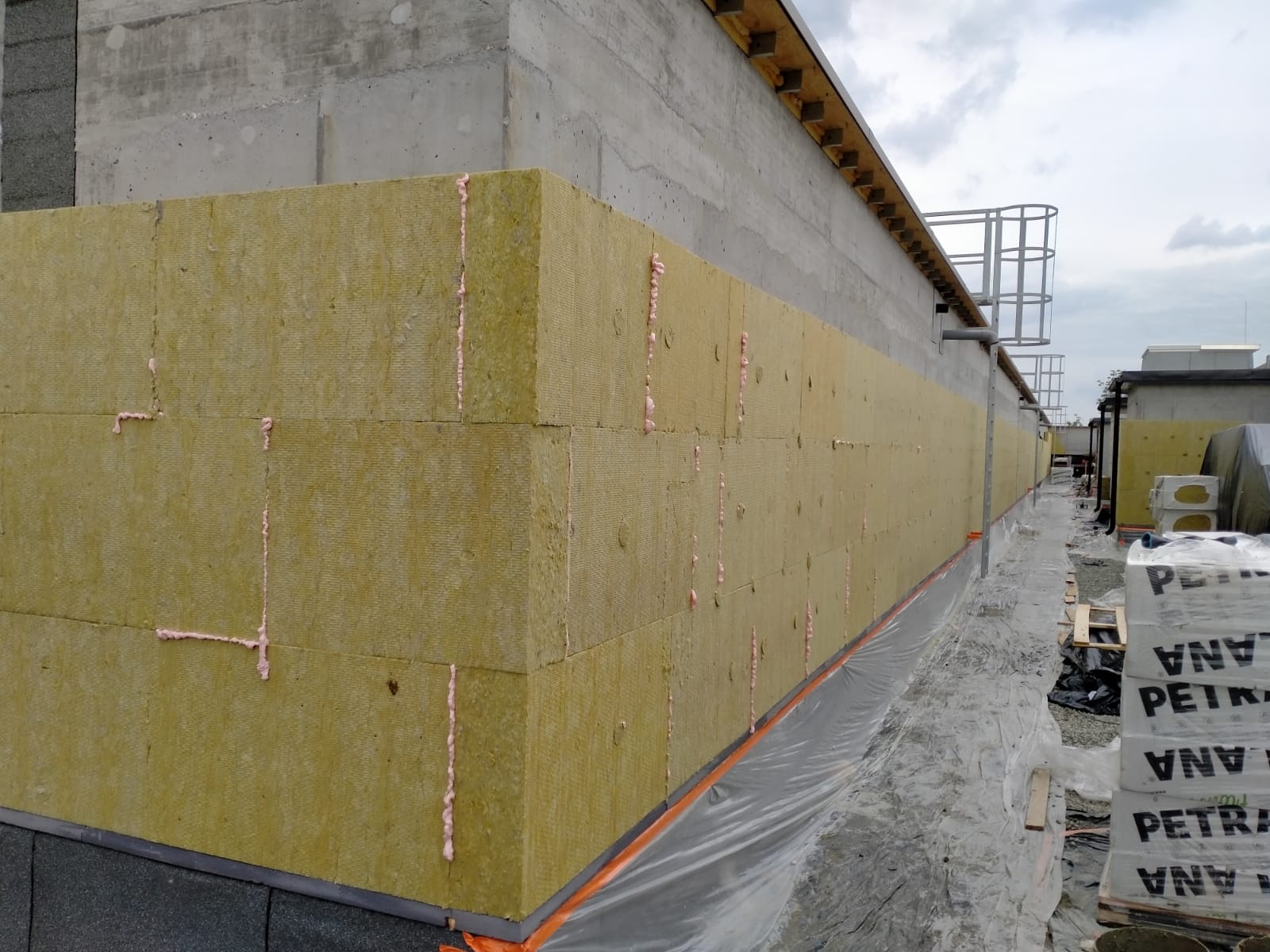 Ocieplanie elewacji budynku wełną mineralną, widoczne płyty izolacyjne z pianką montażową, przygotowane do dalszych prac wykończeniowych.