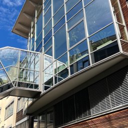 Langteam - Nowoczesny budynek biurowy z przeszkloną fasadą i łącznikiem, odbijający błękitne niebo. Widoczne drewniane elementy elewacji i żaluzje okienne.