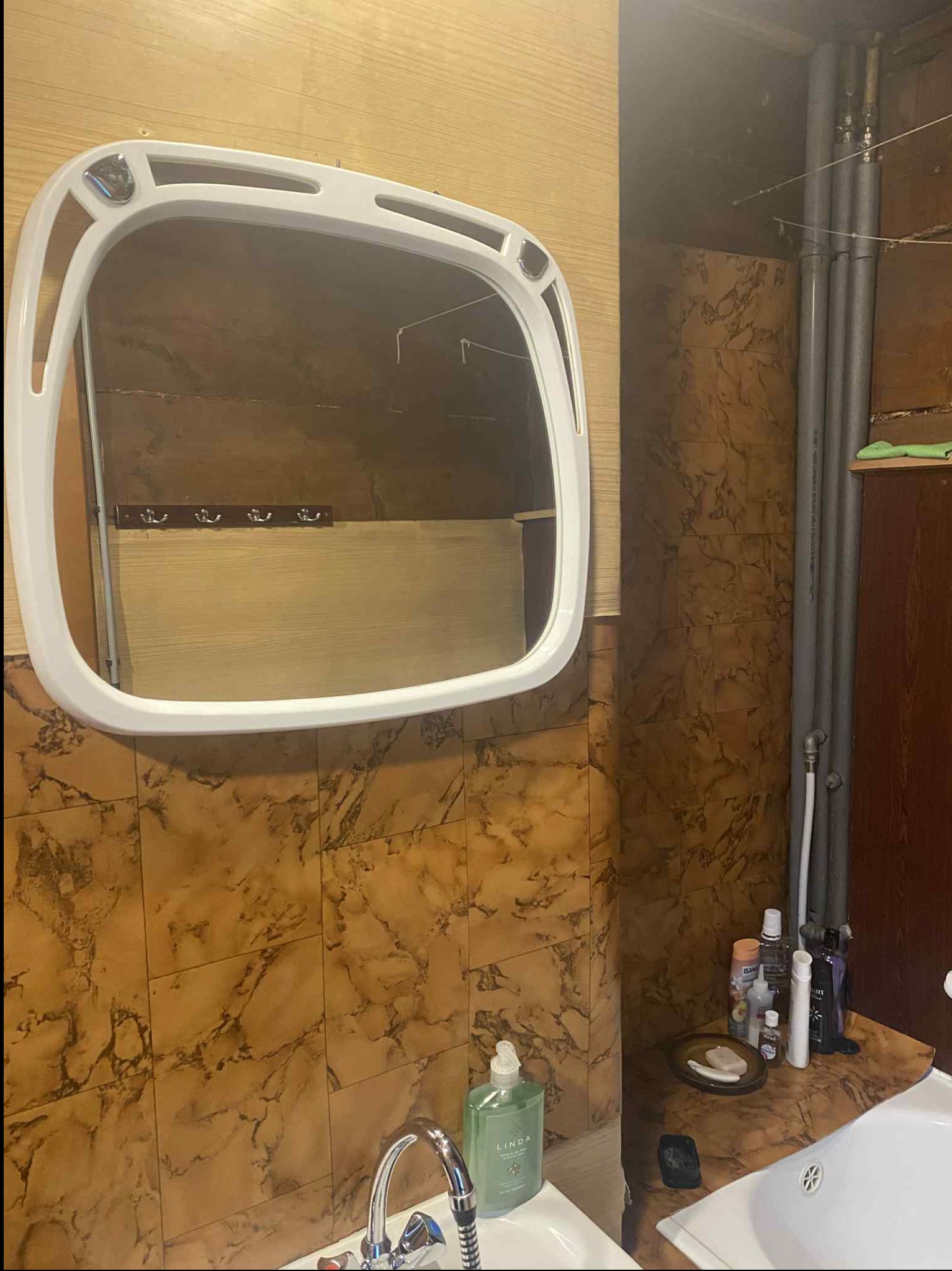 Ukończona łazienka z brązowymi płytkami imitującymi marmur, białą umywalką i lustrem w białej ramie. Widoczne rury i akcesoria łazienkowe.