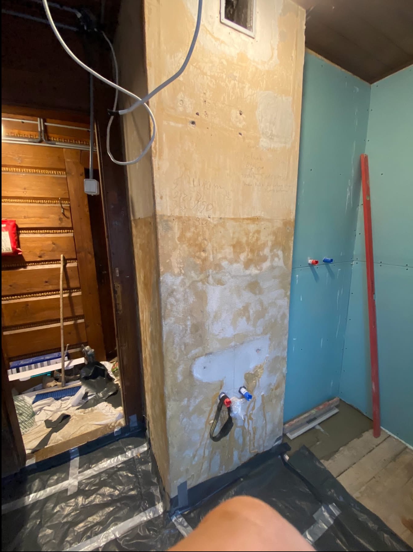 Remont łazienki: stara ściana z instalacją wodną obok nowej ściany z płyt karton-gips, poziomica oparta o ścianę. Podłoga zabezpieczona folią.
