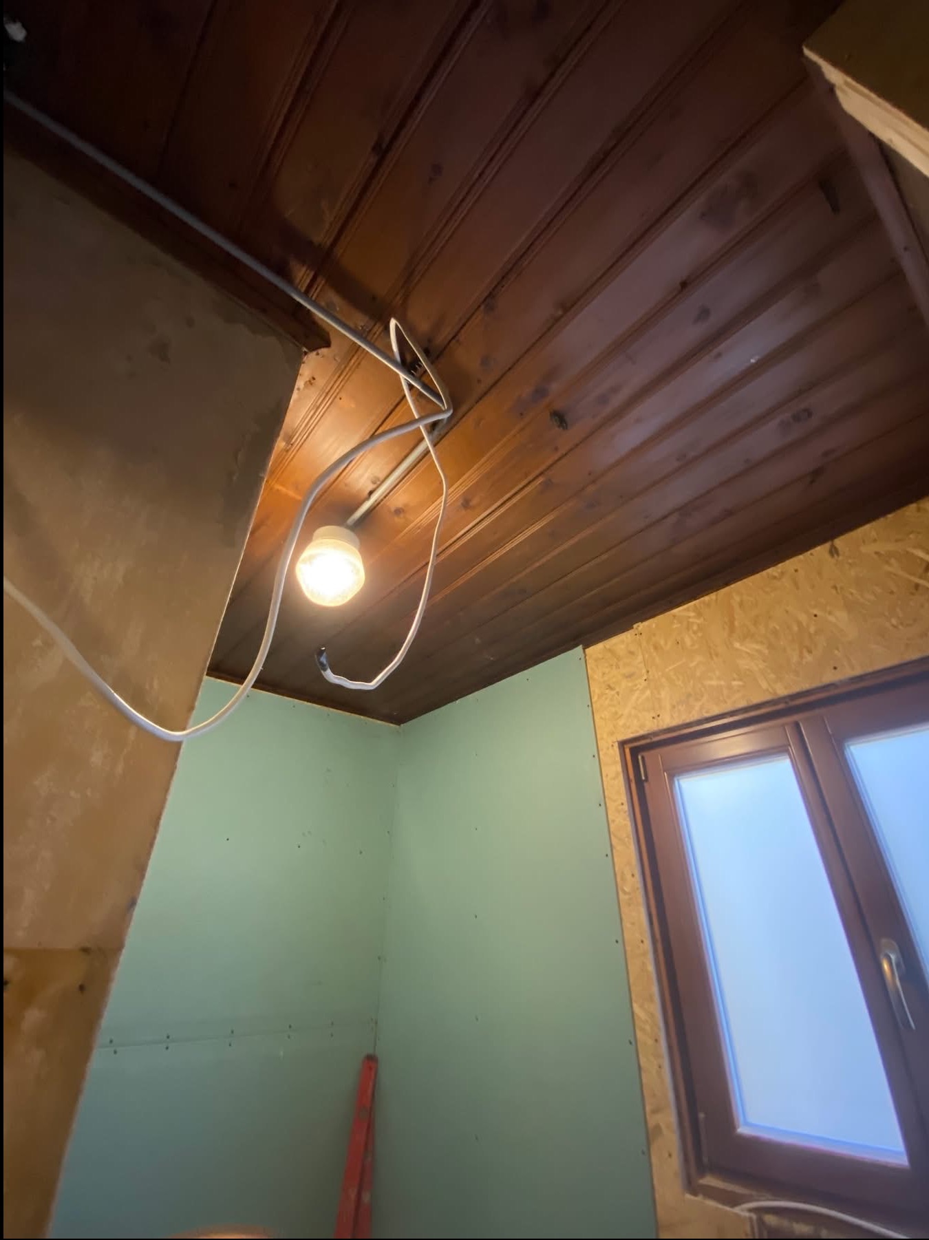 Montaż płyty karton gips na ścianach poddasza z drewnianym sufitem i oknem. Widoczne przewody elektryczne i poziomica.