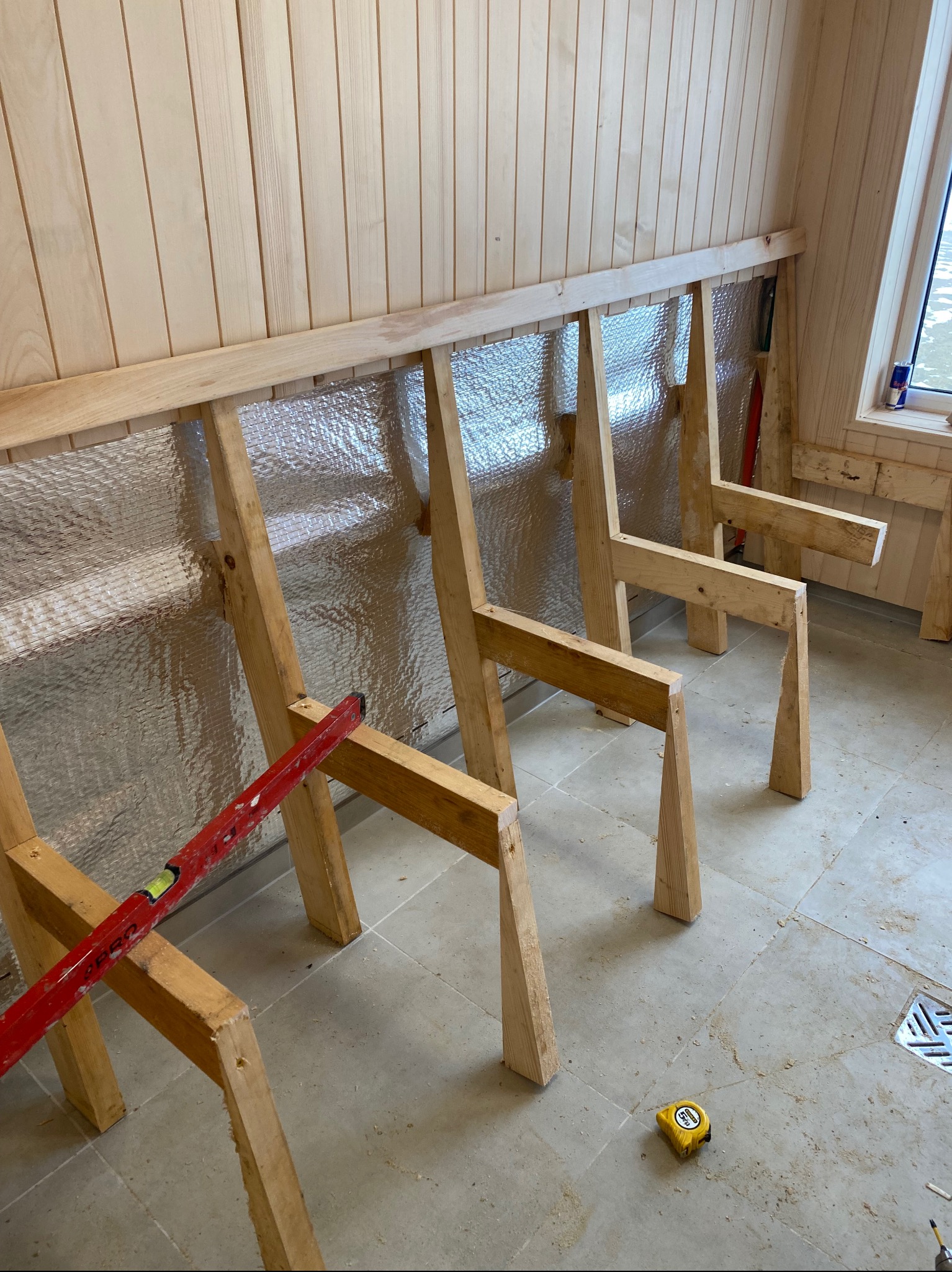 Konstrukcja drewniana przy ścianie z izolacją, poziomica i miarka na podłodze. Budowa szkieletu pod płytę karton gips, widok z bliska.