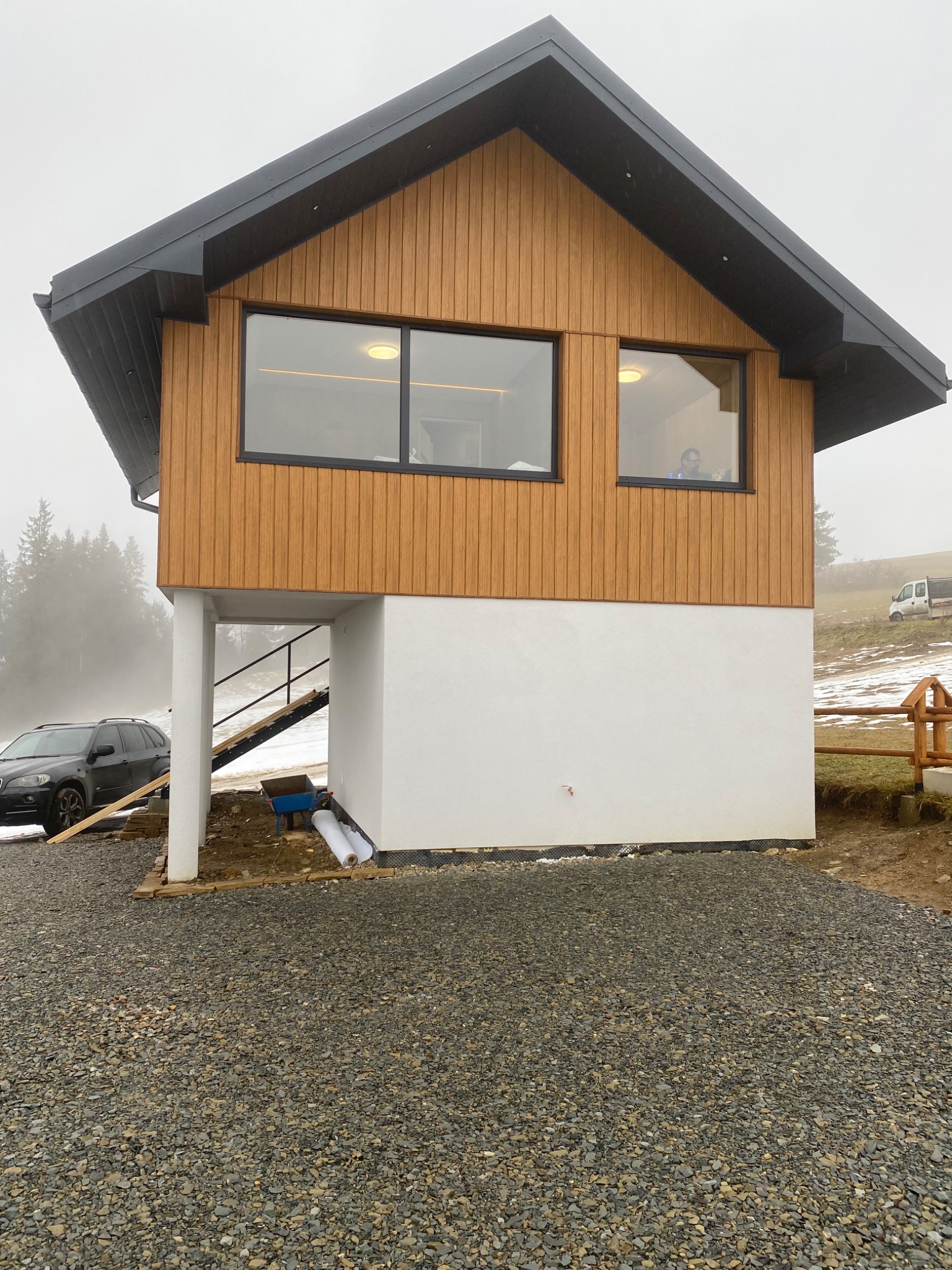 Nowoczesny dom z elewacją z drewnianych paneli w Poroninie. Widoczne okna, biały parter i szara dachówka. Na pierwszym planie utwardzony teren.