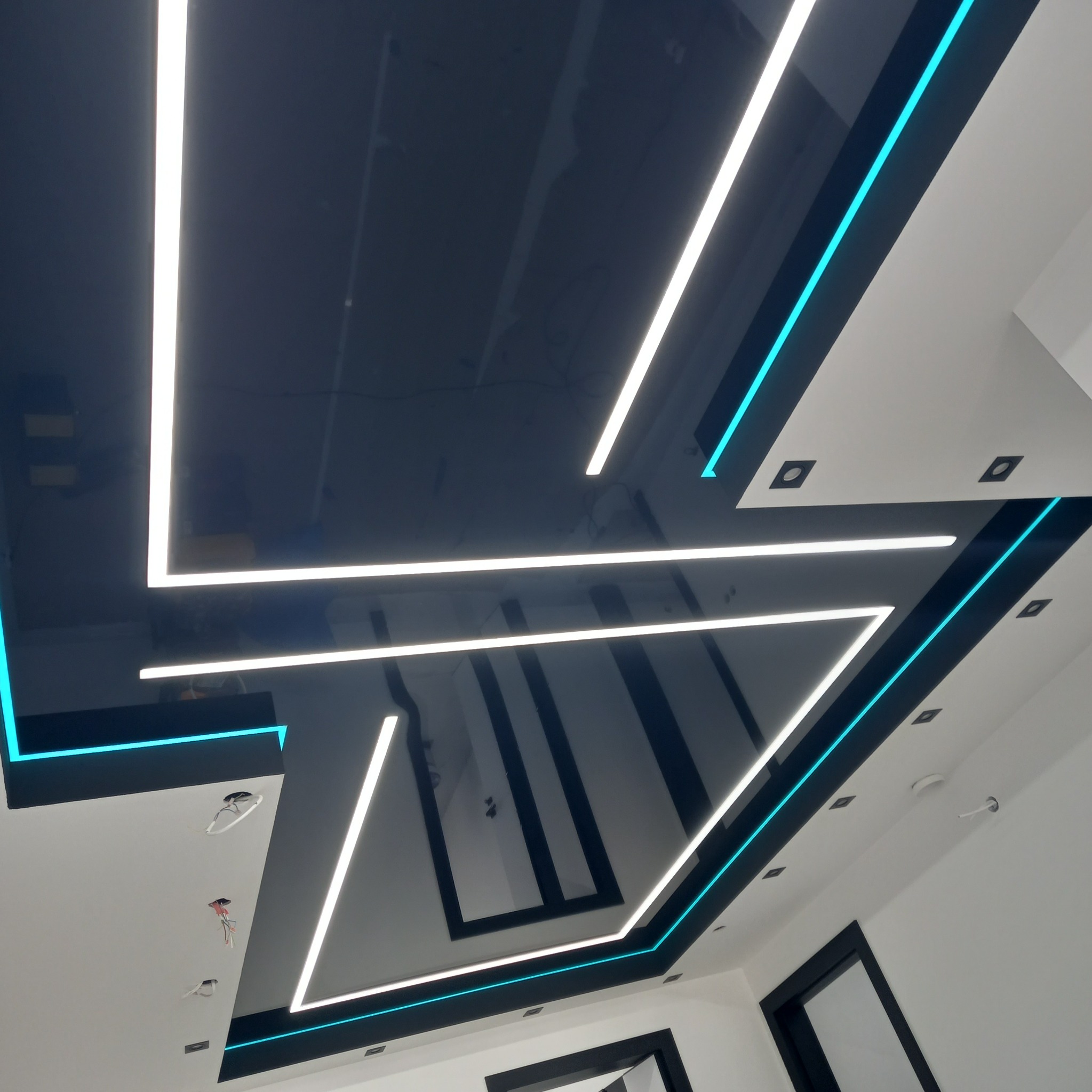 Czarny, błyszczący sufit z geometrycznym układem białych i turkusowych linii LED, tworzących nowoczesny design. Widoczne punkty świetlne w białej części sufitu.