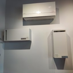 Winenergy - Trzy białe jednostki klimatyzacyjne Mitsubishi, różne modele, zamontowane na jasnej ścianie. Widoczne oznaczenia modeli: VL-100EUS i VL-50SR2, VL-50S2.