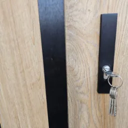 Klucze w zamku nowoczesnych drzwi z drewnianą okleiną i czarnymi elementami dekoracyjnymi. Detal zamka i kluczy.