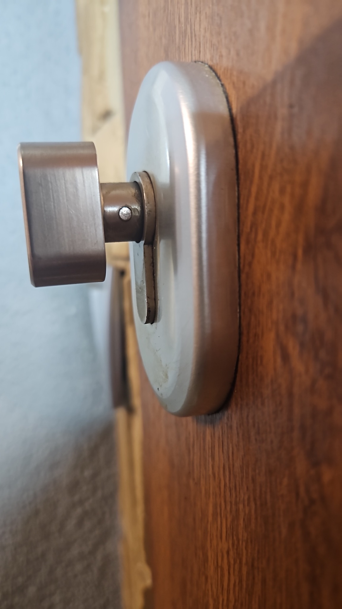 Szczegółowe ujęcie klamki z metalu na drewnianych drzwiach, widoczny mechanizm zamka. Delikatne oświetlenie podkreśla fakturę drewna i metalu.