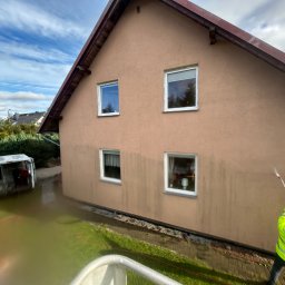 Maciej Ellwart - Pracownik w jaskrawej kurtce czyści elewację domu za pomocą myjki ciśnieniowej. Widoczny fragment elewacji przed i po czyszczeniu, oraz zaparkowany bus firmy.