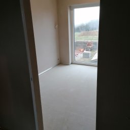 Tynki Spider - Wnętrze pokoju po wylaniu posadzki, ściany przygotowane do malowania. Widoczne okno z widokiem na zewnątrz i fragment drzwi.