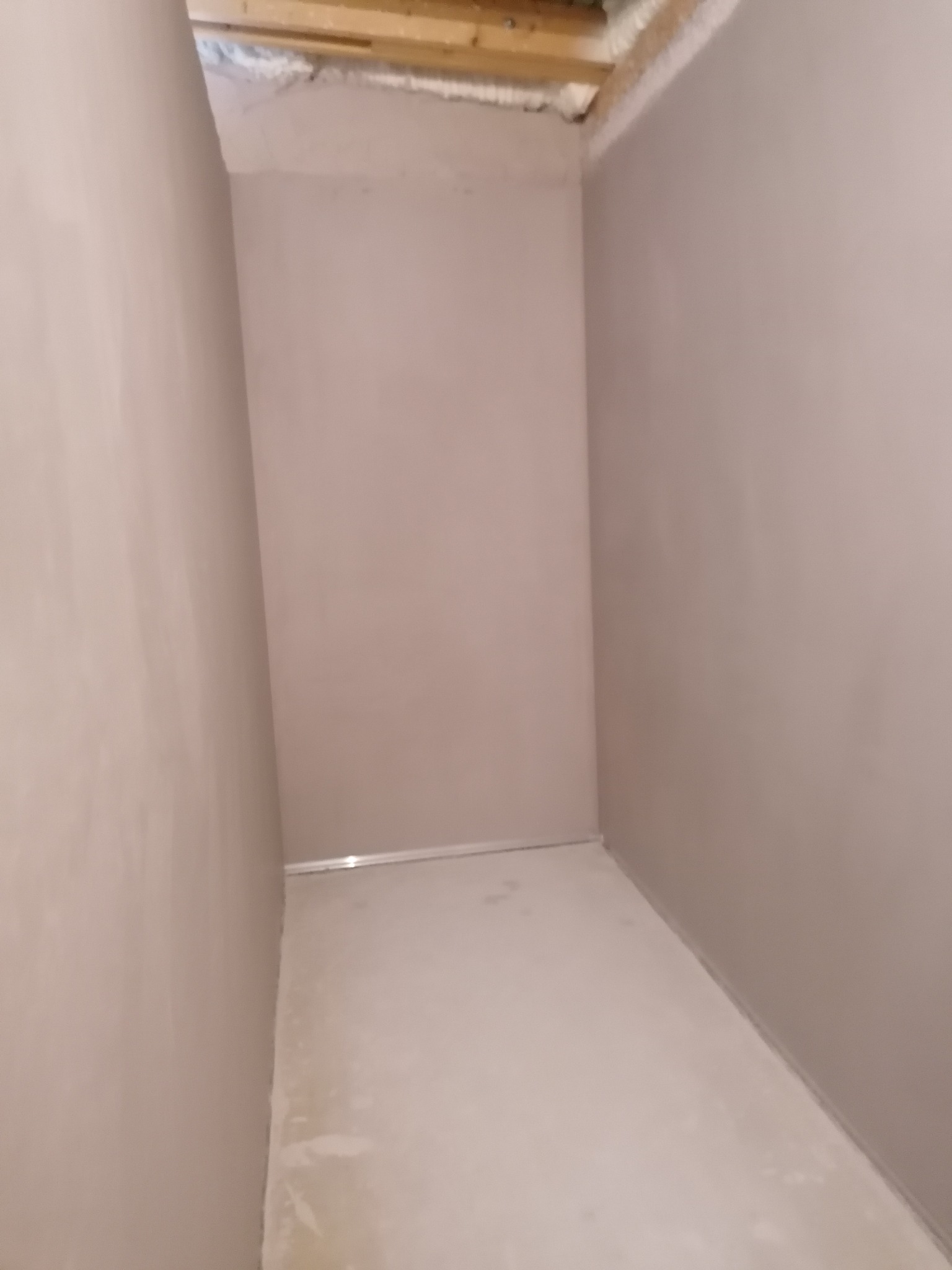 Wnętrze pokoju po nałożeniu gładzi, widoczne gładkie ściany w odcieniach beżu i szarości, przygotowane do dalszych prac wykończeniowych. Widoczny fragment sufitu z drewnianą konstrukcją.