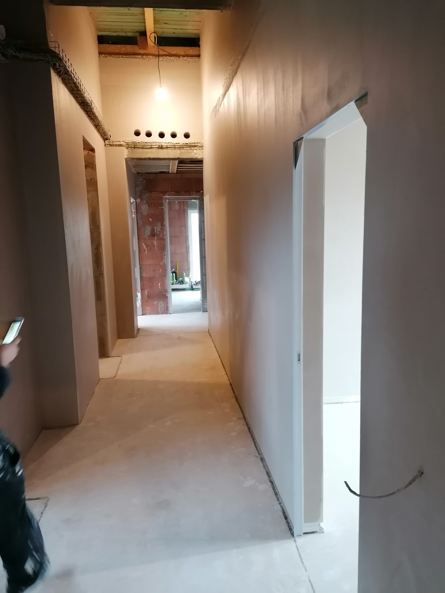 Korytarz w trakcie prac wykończeniowych: ściany pokryte gładzią, widoczne otwory na oświetlenie, surowy beton na podłodze, częściowo zamontowane ościeżnice.