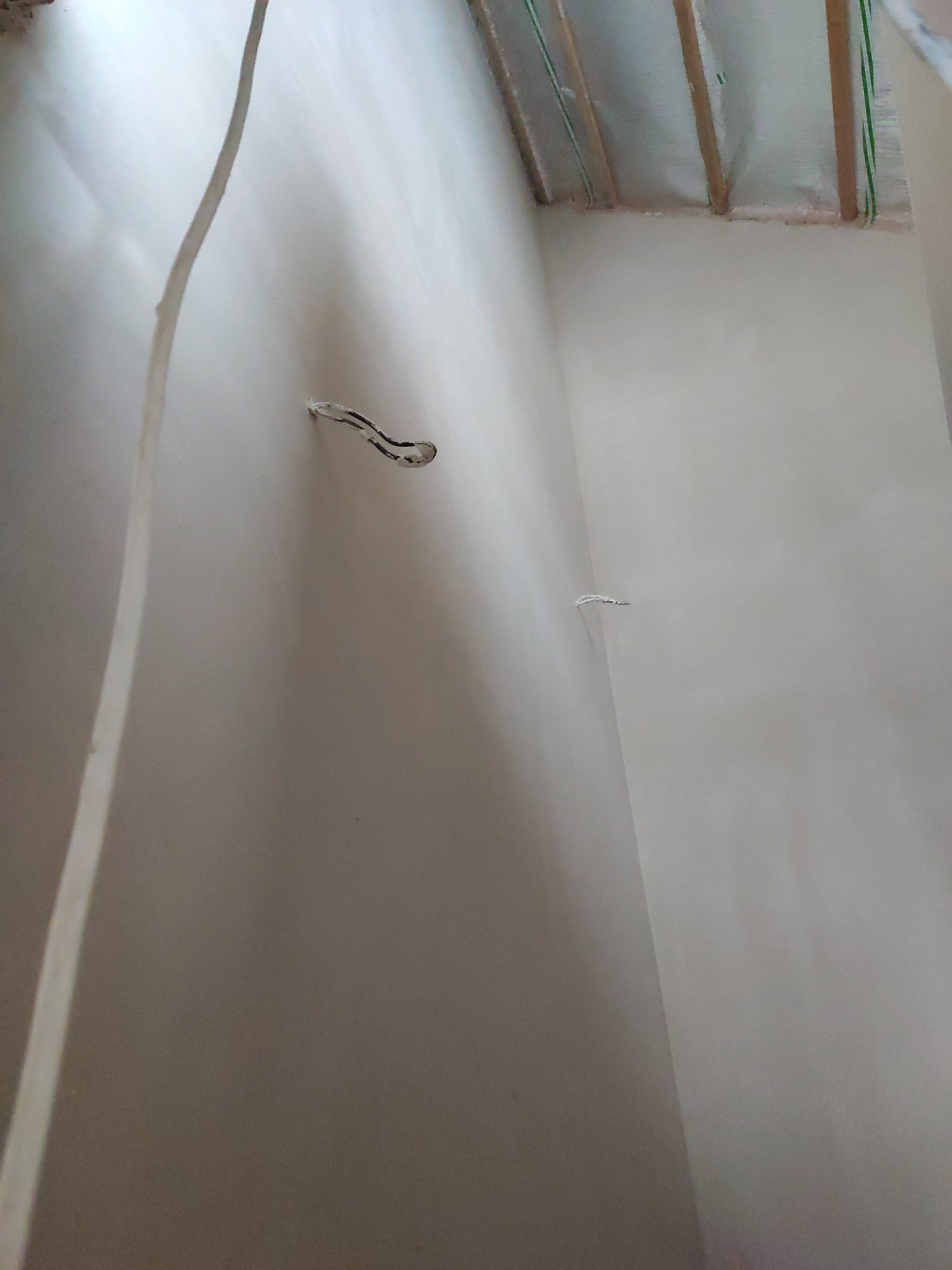 Świeżo położone gładzie na ścianach w rogu pomieszczenia, widoczne wystające kable elektryczne i fragment ocieplonego poddasza. Jasne, neutralne kolory.