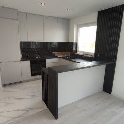 Serhii Kalataliuk - Nowoczesna kuchnia z szarymi szafkami, czarnym blatem i marmurową podłogą. Wyspa kuchenna z drewnianymi lamelami dodaje elegancji. Jasne wnętrze z oknem.