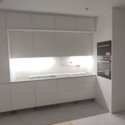 Serhii Kalataliuk - Minimalistyczna, biała kuchnia na wymiar z podświetleniem LED pod szafkami wiszącymi. Widoczne zabudowane piekarniki i marmurowa podłoga.