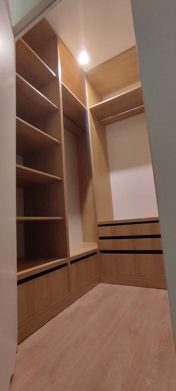 Jasna, drewniana garderoba z półkami i szufladami, oświetlona punktowo, z widoczną podłogą z paneli. Ujęcie z wnętrza, podkreślające funkcjonalność i estetykę.