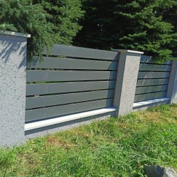 Bartłomiej Monica OGRO-TECH - Nowoczesne ogrodzenie z szarych, poziomych paneli i betonowych słupków. Elementy drewniane dodają ciepła. Trawa i zieleń w tle.