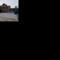 Bartłomiej Monica OGRO-TECH - Nowoczesne, czarne ogrodzenie panelowe z bramą wjazdową na posesję z kostką. Widoczny fragment domu z czerwonej cegły w tle.